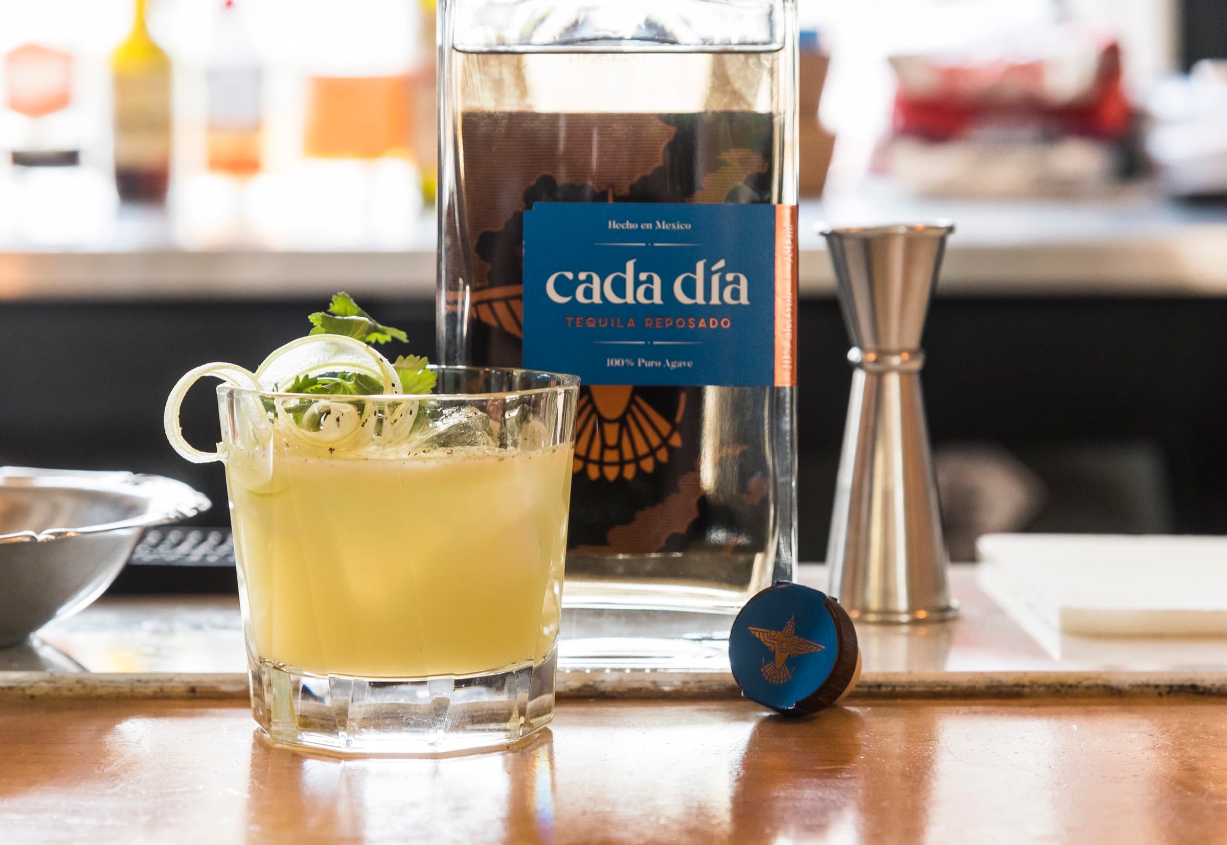 A Cada Día cocktail served alongside the bottle at a bar