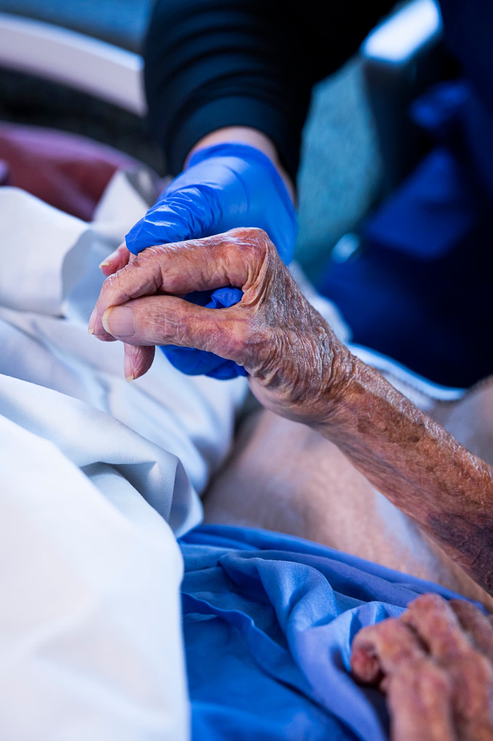 A caregiver holding an elderly patient's hand at St. Joe's